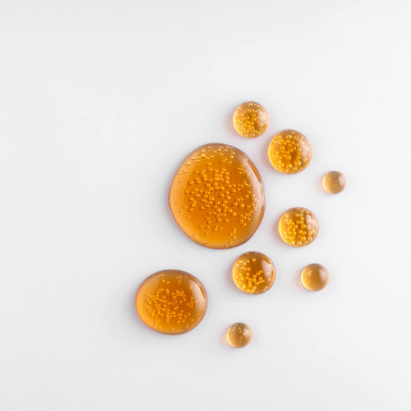 Round golden drops of oil or serum on white background, retinol, vitamin C serum droplets