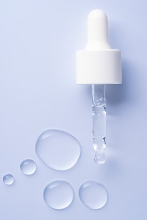 close up of pipette with pouring liquid serum drops with soft shadows on blue background. Trendy...