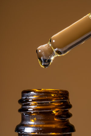 macro shot of serum dropper pipette and pouring retinol beauty serum on brown background. Skin care treatment presentation. texture of the productの写真素材