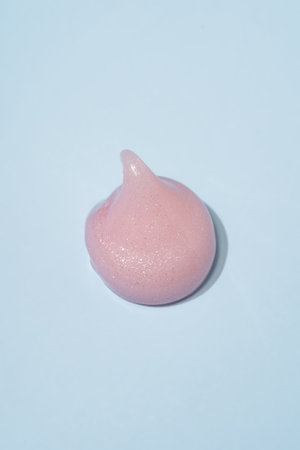 Close-up shot of pink liquid cosmetic gel or serum drop with a glossy, shiny texture on a smooth...
