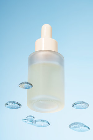 Glass dropper bottle of cosmetic product with serum on a glass shelf and water drops on a blue background, bottom view. Skin care conceptの写真素材