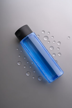 Face hyaluronic toner or essence in blue bottle on gray background with drops of water. Unbraiding packaging presentation. Mockup for designersの写真素材