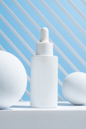 Facial serum in glass dropper bottle on white podium and balls on blue background. Natural skin care cosmetic. Beauty routine concept. Minimal composition. Trendy product for branding.の写真素材