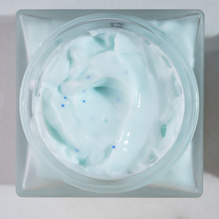 top view of frosted glass jar with collagen face cream. Skincare concept on blue background with strong shadows. Natural cosmetic concept for face body care.の写真素材
