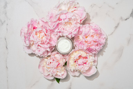 Cosmetic cream with fresh flowers of pink peony blossoms on light marble background. Dermatologic, components for cosmeticsの写真素材