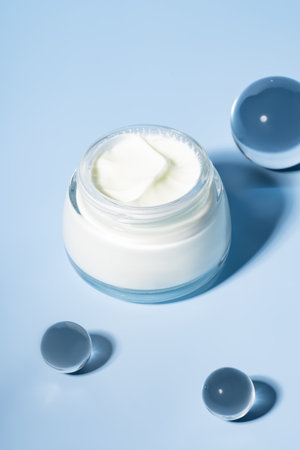 Open cream jar with glass cooling balls on vibrant blue background. A fresh, luxurious skincare flat lay for spa brands and product texture visualsの写真素材