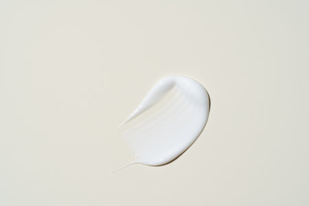 Smooth, glossy cream streak on muted beige, capturing its high-shine finish and rich hydration for premium beauty campaigns.の写真素材