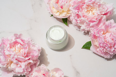 Professional product shot of open cream jar with peony accent, highlighting formula texture for e-commerce and packaging design content.の写真素材