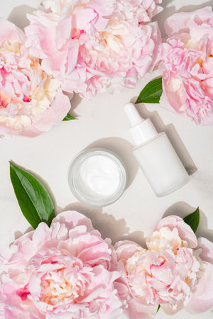 Serum bottle and cream jar arranged on a tray with blooming peony, creating a luxurious floral skincare aesthetic. Elegant flat lay for beauty brands and serene self-care visuals.の写真素材