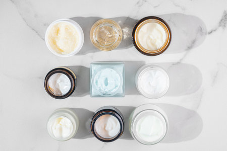 Overhead shot of multiple open skincare jars displayed on a table, creating an aesthetic flat lay. Perfect for beauty brand promotions, product catalogs, and social media contentの写真素材