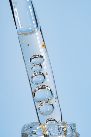 Close-up of a cosmetic pipette precisely pouring golden serum into glass bottle. Clean beauty lab aesthetic showcasing skincare formulation and luxury organic productsの写真素材