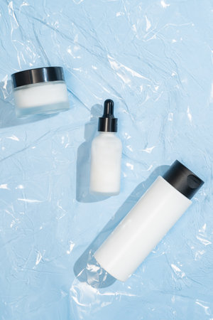 A minimalist white dropper bottle and cream jar elegantly displayed on plastic cellophane, showing clean skincare packaging. The sleek design conveys luxury and purity, perfect for beauty brandsの写真素材