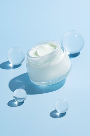 Open cream jar with glass cooling balls on vibrant blue background. A fresh, luxurious skincare flat lay for spa brands and product texture visualsの写真素材