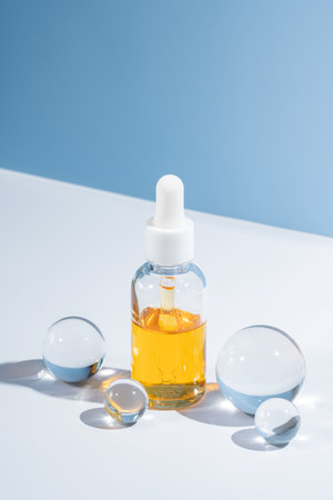 Premium glass dropper bottle with hydrating serum on blue backdrop, accented by glass cooling spheres. Elegant beauty mockup for high-end skincare branding and organic cosmeticsの写真素材
