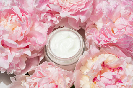 Open cream jar with pink peonies on soft backdrop. Fresh, floral beauty flat lay for skincare brands and feminine product visuals.の写真素材