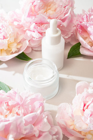 Skincare duo with pink peonies: glass serum bottle and cream jar. Feminine, elegant product shot for natural beauty visualsの写真素材