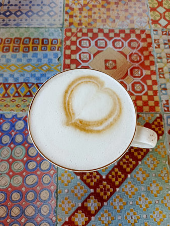 Coffee cup with delicate latte foam art on vintage table with decorative tile coffee break sceneの写真素材