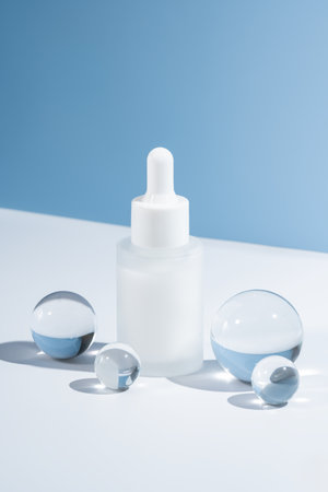 Mockup of glass dropper bottle with face serum or essential oil on blue background with glass balls. The concept of beauty cosmetics, natural products for moisturizing and restoring the skin.の写真素材