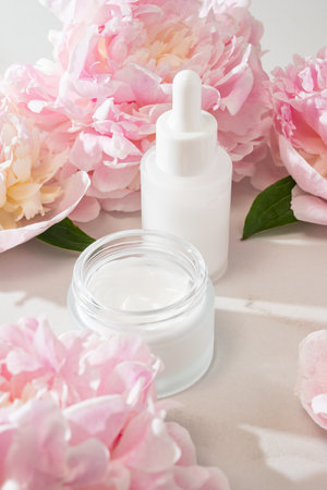 Skincare product display with cream jar, serum bottle and peony accent, ideal for e-commerce visuals, beauty shop catalogs and product showcase content.の写真素材