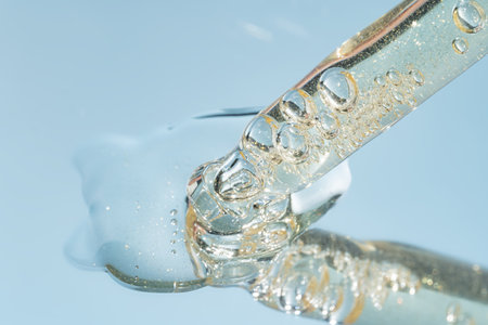 close up of pipette with pouring liquid serum and shadows on blue background. Trendy cosmetics shot with hard shadows.の写真素材