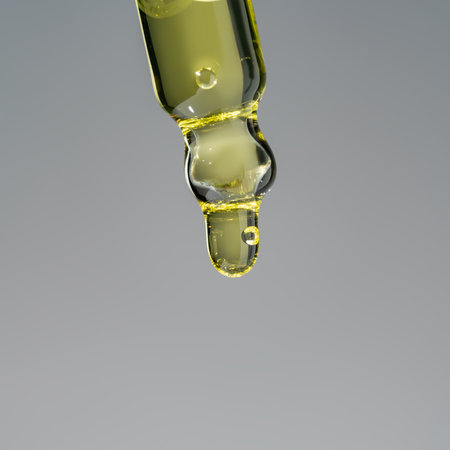 Oily drop dripping from pipette into cosmetic bottle close up, isolated on gray background. skin care product presentationの写真素材