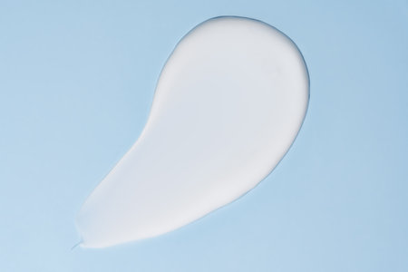 Texture of white cream on blue background. Smear of moisturizer close up. Lotion swatch. Beauty skin...