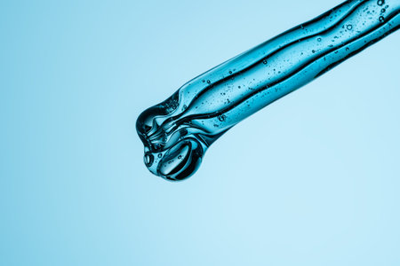 Pipette and drops and smears of cosmetics. Liquid blue gel or a drop of serum on blue background.