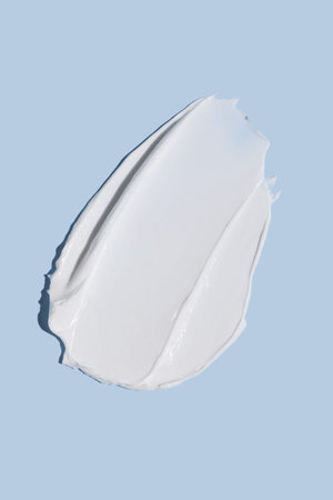 Texture of white cream on blue background. Smear of moisturizer close up. Lotion swatch. Beauty skin...