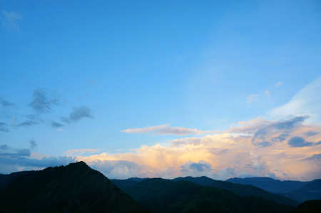A countryside view in the afternoon. Blue sky, orange clouds, yellow clouds and silhouette of mountains. An image with blue copy space for text or message.の写真素材