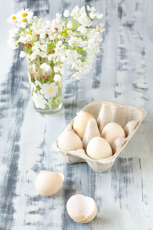 Eggs in a box on a white and gray background. White flowers in the back.