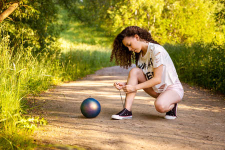 The girl with the ball is tying shoelaces on the road.の写真素材