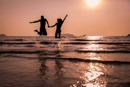 A pair of young people jumping into the sea. Silhouette at sunset.の写真素材