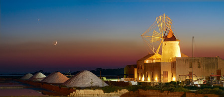 A spectacular conjunction of Moon, Venus and Jupiter over and old salt factory. In the foreground can be seen the salt mounds, the wind mill and the sumps where the sea water is evaporated to recover the crystalized salt.の写真素材