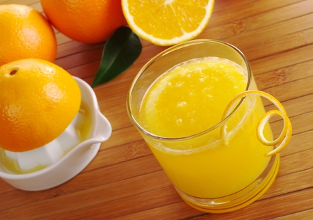 Fresh orange juice with orange slice in glass with squeezer and oranges in background on table mat (Selective Focus)の写真素材