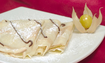 Palatschinken (Pancakes, Crepes) with chocolate and powdered sugar on a plate and a physalis fruit as decorationの写真素材