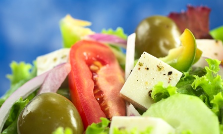 Greek salad out of cheese, green olives, tomato, green bell pepper, red onion, cucumber and lettuce with blue background (Selective Focus, Focus on the cheese) の写真素材