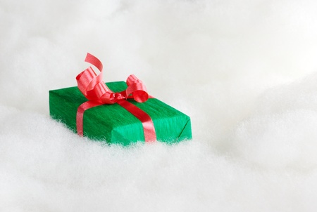 Green Christmas gift with red ribbon on white cotton that looks like clouds (Selective Focus, Focus on the first half of the gift box)の写真素材