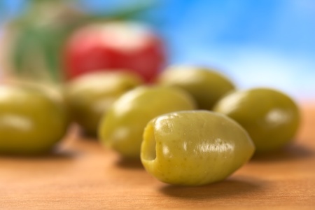 Green olives on wood with blue background (Very Shallow Depth of Field, Focus on the front close to the opening of the front olive)の写真素材