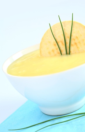 Fresh potato cream soup garnished with a cracker and chives on bluish background (Selective Focus, Focus on the cracker and the chives) の写真素材