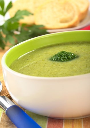 Cream of broccoli garnished with a broccoli floret on top with baguette slices and parsley leaves in the back (Selective Focus, Focus on the broccoli floret on the soup)の写真素材