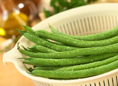 Fresh raw green beans sprinkled with water in white plastic strainer (Selective Focus, Focus on the bean in the middle)の写真素材