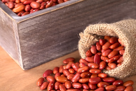 Raw red kidney beans in jute sack and wooden box (Selective Focus, Focus on the beans at the opening of the sack)の写真素材