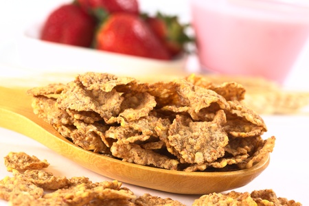 Wholewheat flake cereal on wooden spoon with fresh strawberries and strawberry yogurt in the back...