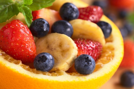 Fresh fruit salad made of banana, strawberries and blueberries in a bowl made of a half orange...