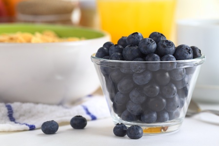 Fresh blueberries in glass bowl with a bowl of cereal, orange juice and cup in the backの写真素材
