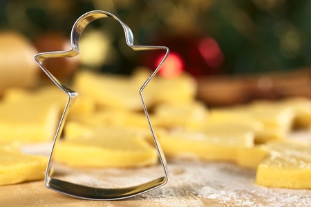 Angel-shaped cookie cutter with raw cookies and Christmas decoration in the back (Selective Focus, Focus on the front edge of the cutter)  の写真素材