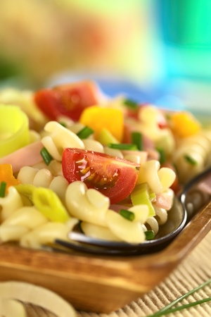 Pasta salad with leek, cherry tomato, yellow bell pepper and ham garnished with chives (Selective Focus, Focus on the tomato in the front)の写真素材