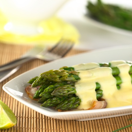 Cooked green asparagus on fried bacon with Hollandaise sauce on top (Selective Focus, Focus on the three asparagus tips in the front)の写真素材