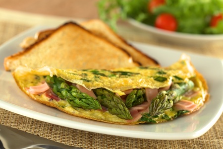 Green asparagus and ham omelet with toast bread and a fresh salad in the back (Selective Focus, Focus on the three asparagus tips in the front)の写真素材