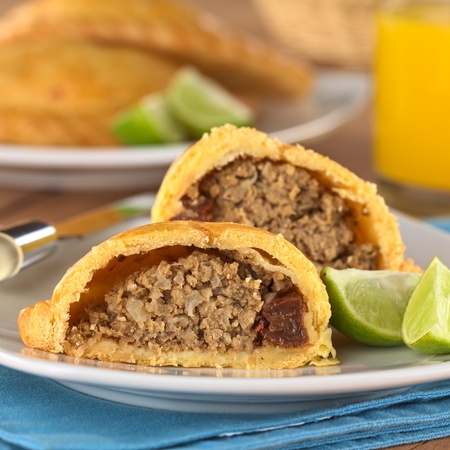 Peruvian snack called Empanada (pie) filled with beef and raisin served with limes (Selective Focus, Focus on the empanada stuffing in the front)の写真素材
